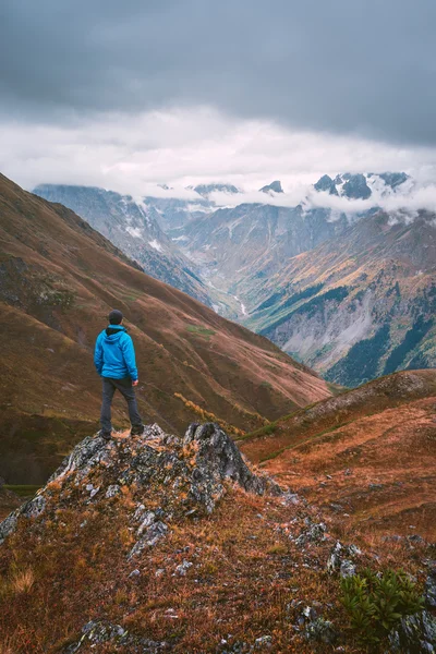 Турист в синей куртке, стоящий на скале в горах — стоковое фото