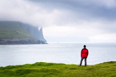 Bir turist Faroe Adaları 'ndaki Vagar Adası' ndaki Trollkonfingur veya Cadıların Parmakları kayalarına bakar.