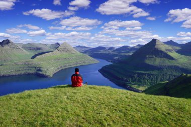 Funningur fiyort manzarası ve Faroe Adaları 'ndaki Eysturoy Adası' ndaki dağlar. Kırmızı ceketli bir turist güneşli bir günde güzel kuzey manzarasının tadını çıkarıyor.