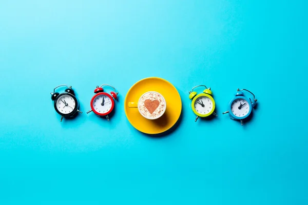 Yellow cup of coffee and colorful clocks — Stock Photo, Image
