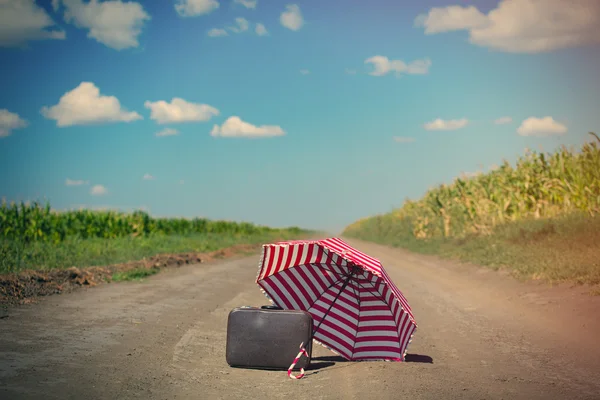 Suitcase and umbrella on the countryside road — Stock Photo, Image