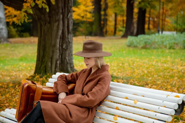 Stylowa Dziewczyna Brązowym Płaszczu Walizką Siedzącą Ławce Jesiennym Parku — Zdjęcie stockowe