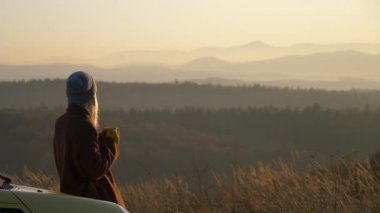 Kız arabanın kaputunda oturuyor ve Beskids dağlarının arkasında elinde bir kupa çay tutuyor.