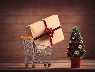 Küçük Noel ağacı ve hediye kutusu süpermarket arabasında ahşap masa ve arka planda