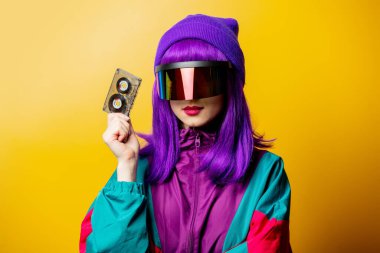 VR gözlüklü ve 80 'lerin eşofmanlı, sarı arka planda ses bandı olan stil kadını.