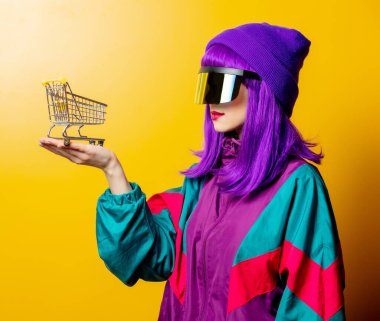 VR gözlüklü ve sarı arka planda alışveriş arabası olan 80 'lerin eşofmanlı stil kadını.