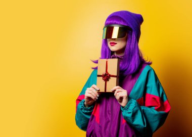 VR gözlüklü ve sarı arka planda hediye kutusu olan 80 'lerin eşofmanlı stil kadını.