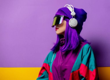VR gözlüklü ve 80 'lerin eşofmanlı, menekşe arka planda kulaklıklı stil kadını.