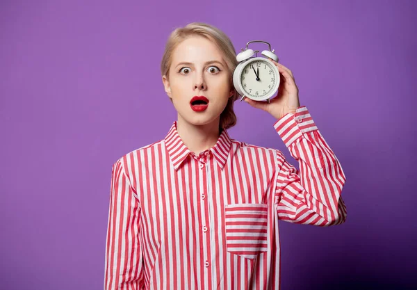 紫の背景に目覚まし時計と赤い縞模様のシャツの美しい女性 — ストック写真