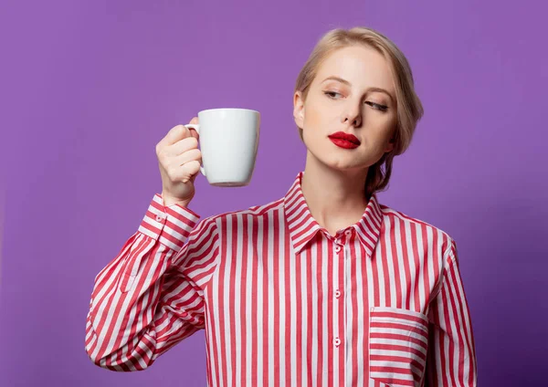 紫の背景にコーヒーのカップと赤い縞模様のシャツの美しい女性 — ストック写真