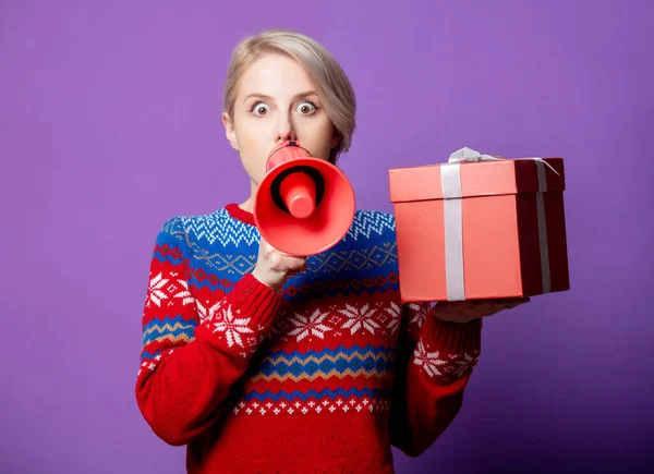 美しい女性でクリスマスセーターでギフトボックスとメガホン上の紫の背景 — ストック写真