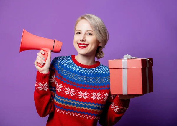 美しい女性でクリスマスセーターでギフトボックスとメガホン上の紫の背景 — ストック写真