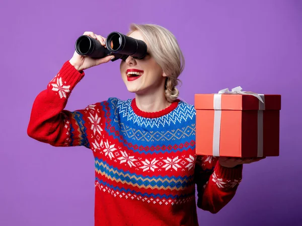美しい女性でクリスマスセーターでギフトボックスと双眼鏡で紫の背景 — ストック写真