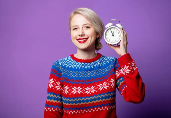 美しいです女性でクリスマスセーターで目覚まし時計上の紫の背景 — ストック写真