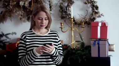 Cep telefonu olan güzel bir kadın Noel süslemeli şöminenin yanında. 
