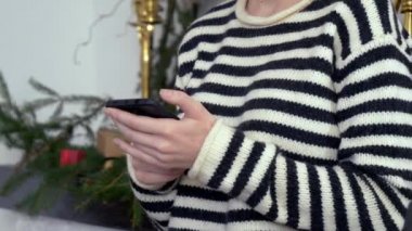 Cep telefonu olan güzel bir kadın Noel süslemeli şöminenin yanında. 