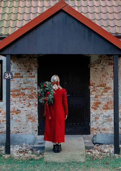 Kırmızı Ceketli Kız Noel Çelengiyle Bir Kapıyı Süslüyor — Stok fotoğraf