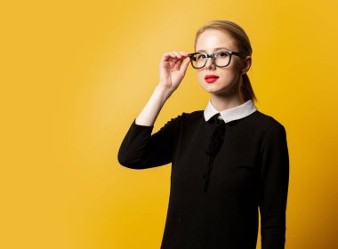 Siyah elbiseli ve sarı arka planda gözlüklü bir kadın. 