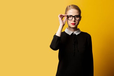 Siyah elbiseli ve sarı arka planda gözlüklü bir kadın. 