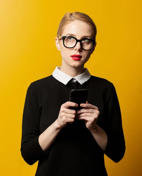 黄色の背景に携帯電話と黒の正式な服のスタイルの女性 — ストック写真