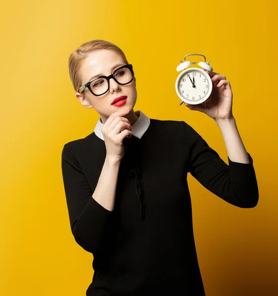黄色の背景に目覚まし時計と黒の正式な服のスタイルの女性 — ストック写真