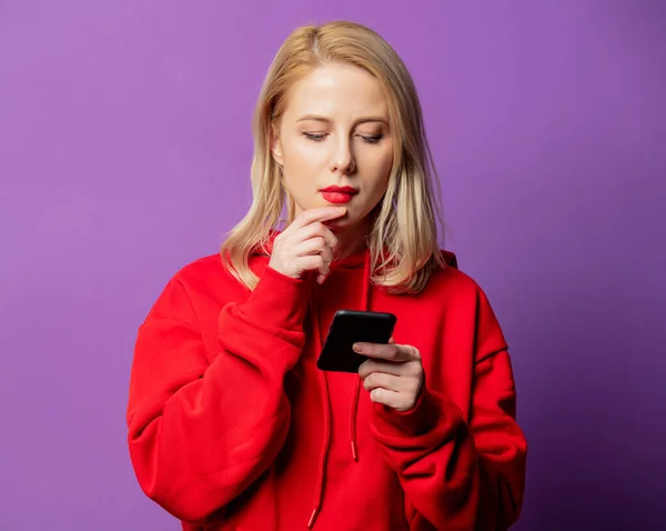 Twijfel Blonde Vrouw Rode Sweater Met Behulp Van Mobiele Telefoon — Stockfoto