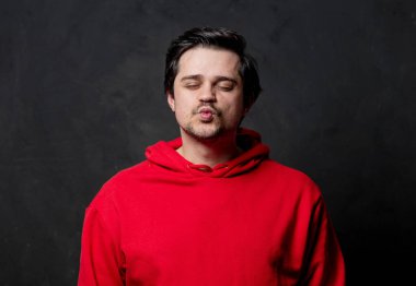 Kırmızı tişörtlü beyaz adam koyu arkaplanda bir öpücük veriyor.