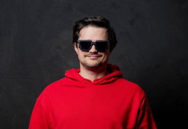 Kırmızı tişörtlü, siyah arka planda güneş gözlüklü beyaz adam.