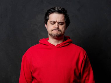 Siyah arka planda kırmızı kazaklı beyaz üzgün adam.