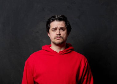 Siyah arka planda kırmızı kazaklı beyaz üzgün adam.