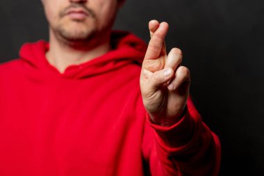 Kırmızı kazaklı beyaz adam arka planda çapraz parmak hareketi gösteriyor.