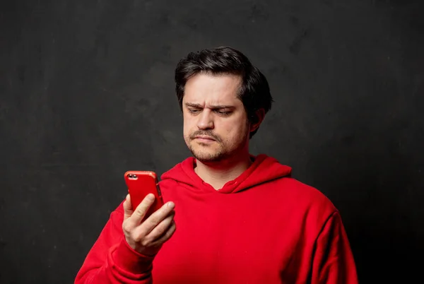 Surprised Guy Red Sweatshirt Looking Mobile Phone Dark Background — Stock Photo, Image