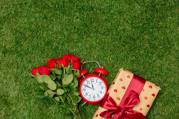 绿草上有红玫瑰花束和装有闹钟的礼品盒 — 图库照片
