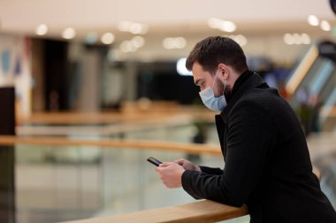 Yüz maskeli ve ceketli adam Salgın zamanında şehir merkezinde cep telefonu kullanıyor. 