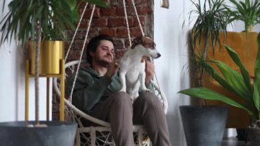 Adamım evde salıncakta sallanan bir köpekle eğleniyor. 