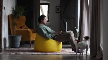 Adam evde aynı anda hem bilgisayarla hem de köpekle oynuyor.