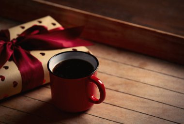 Bir fincan kahve ve hediye paketi ahşap masada. 