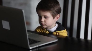 Evdeki masada oturan dizüstü bilgisayara bakan çocuk.