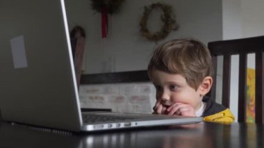 Evdeki masada oturan dizüstü bilgisayara bakan çocuk.