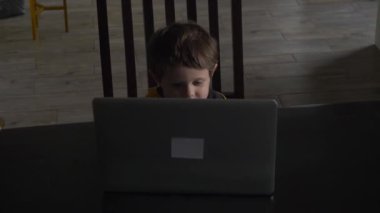 Evdeki masada oturan dizüstü bilgisayara bakan çocuk.