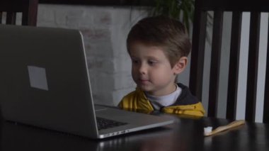 Evdeki masada oturan dizüstü bilgisayara bakan çocuk.