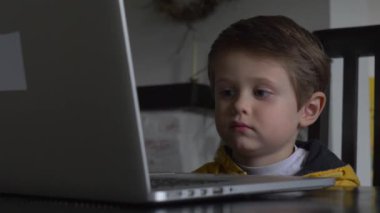 Evdeki masada oturan dizüstü bilgisayara bakan çocuk.