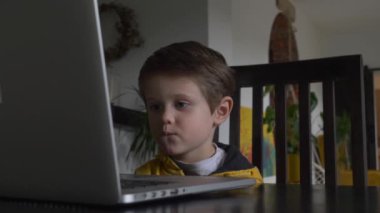 Evdeki masada oturan dizüstü bilgisayara bakan çocuk.