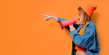 Sarı arka planda pembe megafonlu kot elbiseli genç bir kız. Kadın direnişini sembolize ediyor. 1980 'lerin tarzında kıyafetler.