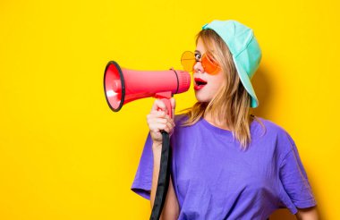 Sarı arka planda pembe megafonlu mor elbiseli genç bir kız. Kadın direnişini sembolize ediyor. 1980 'lerin tarzında kıyafetler.