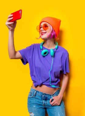 Mor elbiseli, kulaklıklı ve sarı arka planda cep telefonu olan genç bir kız. 1980 'lerin tarzında kıyafetler.