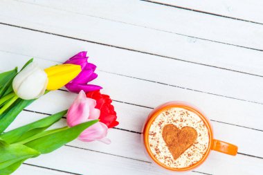 Masadaki lalelerin yanında kalp şeklinde kapuçino..