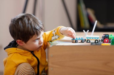 Küçük çocuk evdeki masada tahta trenle oynuyor.
