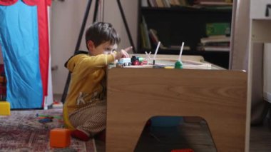 Küçük çocuk evdeki masada tahta trenle oynuyor.