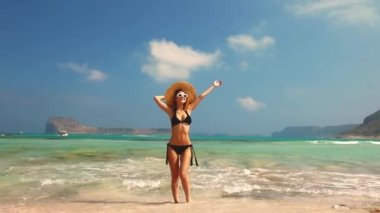 Siyah bikinili ve şapkalı genç kızıl kız Balos sahilinde, batı Girit, Yunanistan. Yaz mevsimi tatili, Temmuz